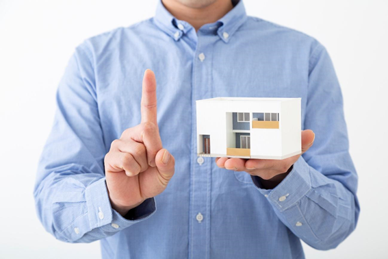 手のひらに住宅の模型を持った男性が人差し指を立てて注意を促している