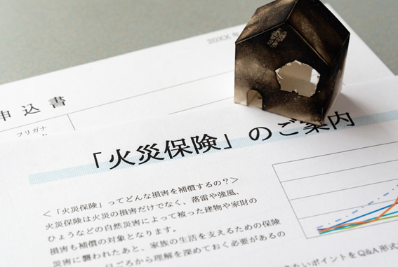 火災保険の書類の上に、焼け焦げた住宅の模型が置いてある